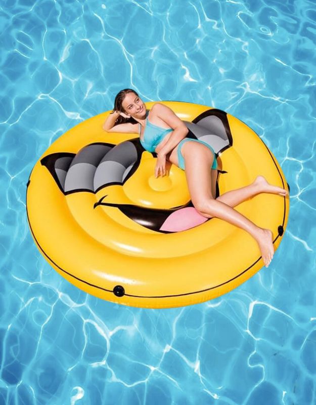 Woman relaxing on Intex Cool Guy Island inflatable pool float with sunglasses emoji design in the water.